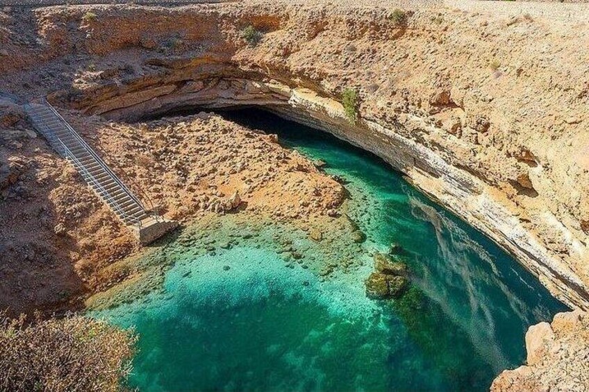 A natural rock formation with a clear blue pool and a wooden bridge. 2