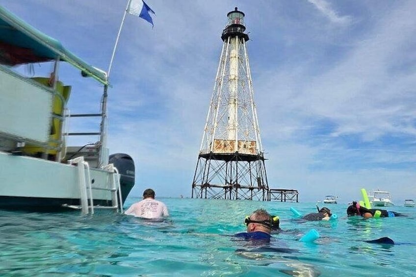People swimming in clear blue water, a lighthouse, and a boat with a flag. 1