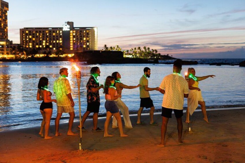 A group of people dancing on a beach at sunset with a cityscape in the background. 2