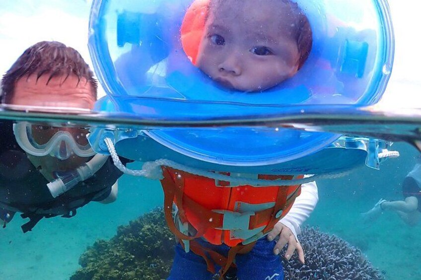 A person underwater with a clear helmet, another person in a diver's suit, and a coral reef in the background. 4
