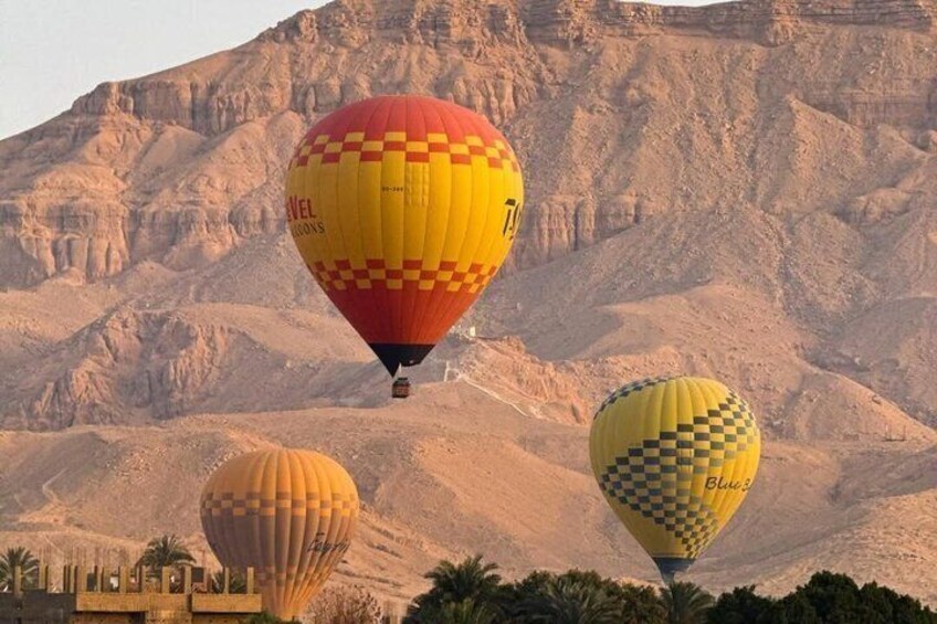 Heißluftballons mit Schachmuster fliegen über eine Wüstenlandschaft mit felsigen Bergen im Hintergrund. 5