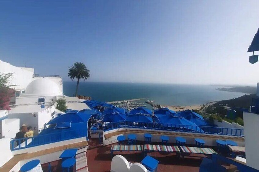 A seaside terrace with blue umbrellas and tables overlooking the ocean. 2