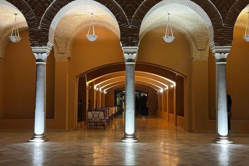 A spacious interior with arched ceilings and columns, featuring a long corridor and seating area. 1