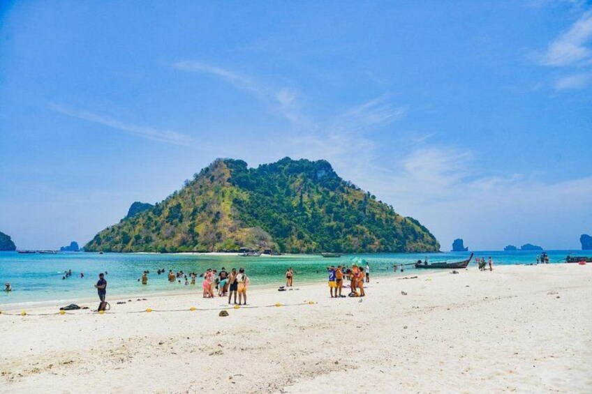 Una playa con gente, barcos y una isla boscosa al fondo. 3