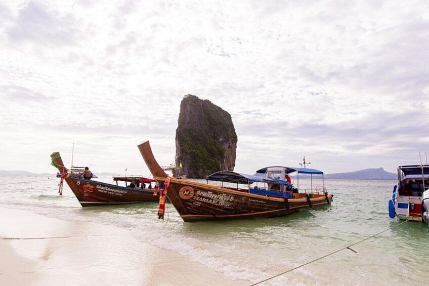 Barcos de madera tradicionales con timones laterales amarrados en una playa, con una destacada formación rocosa al fondo. 5