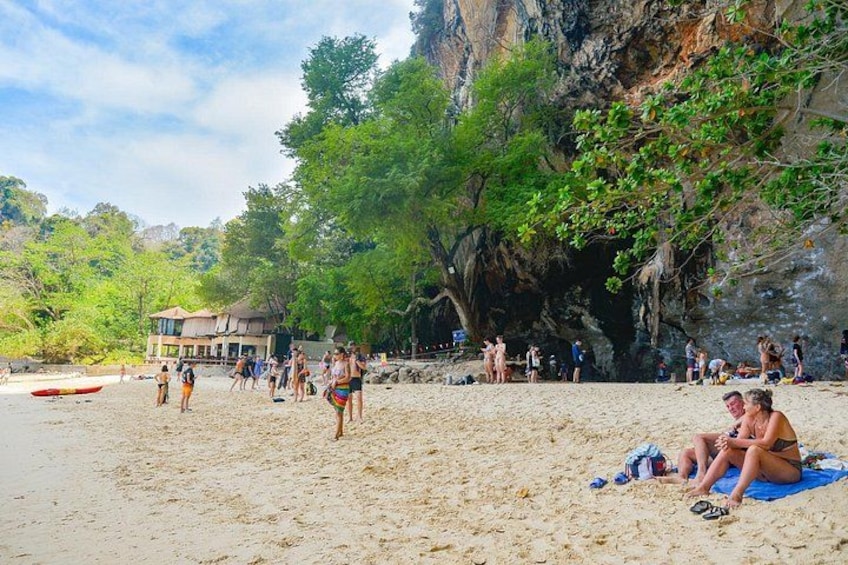 Una playa con gente tomando el sol, un edificio y un acantilado rocoso. 4