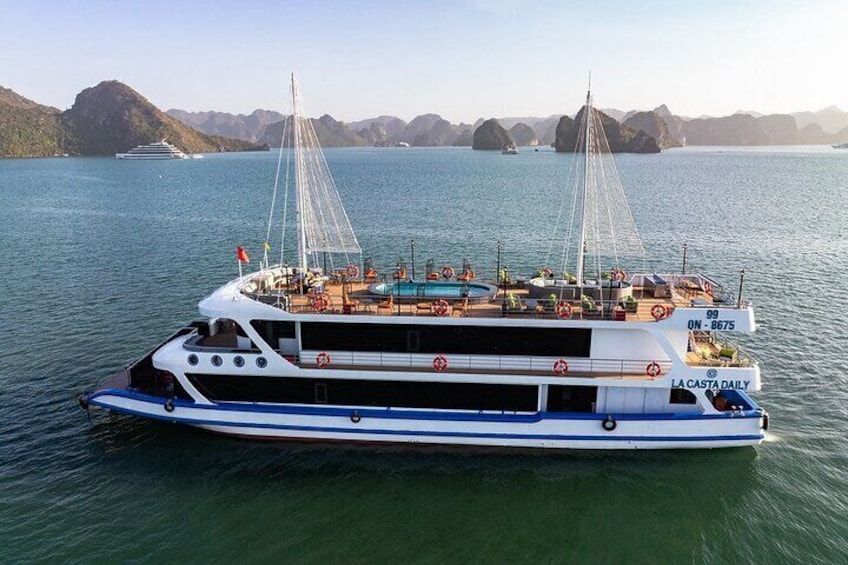 Un'imponente barca chiamata 'La Casta Daily' con una livrea blu e bianca, che naviga su acque calme con un paesaggio montuoso sullo sfondo. 1