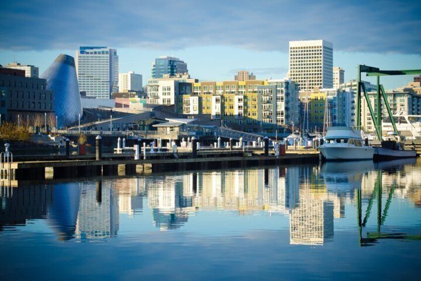 A waterfront cityscape with a distinctive building, a marina with boats, and a bridge. 1