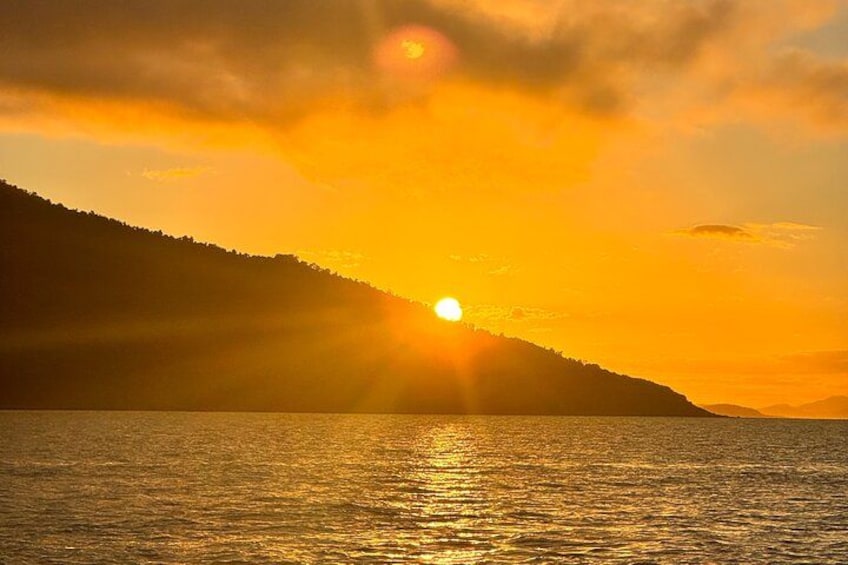 A sunset over a body of water with a mountain in the background. 2