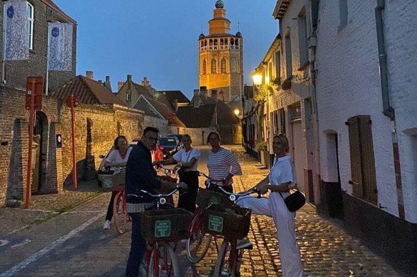 En kullerstensgata med människor på cyklar, historiska byggnader och ett torn i bakgrunden. 3