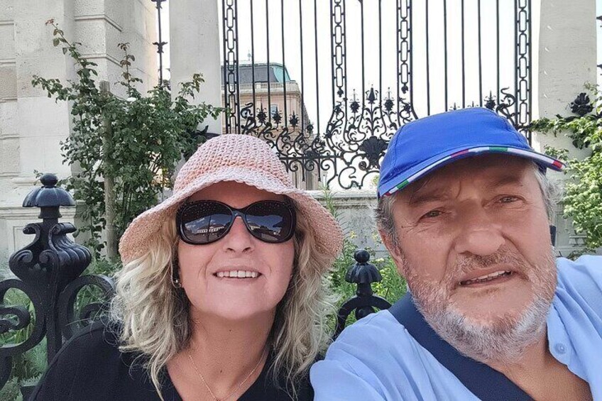 Two people in front of a wrought iron gate with a building in the background. 4
