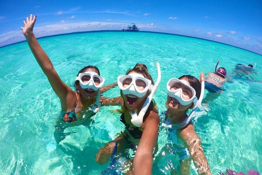 Three people snorkeling in clear turquoise water with a ship in the background. 4