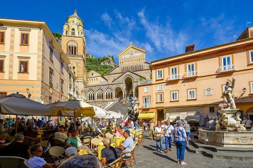 A crowded square with historic buildings, a fountain, and a statue. 3