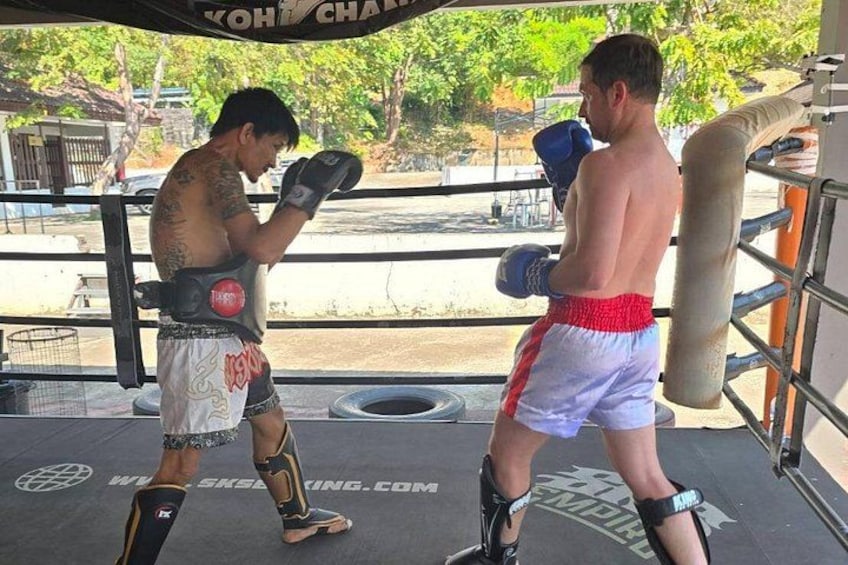 Two individuals in a boxing ring, one wearing red and white shorts and the other in white shorts with red trim. 1
