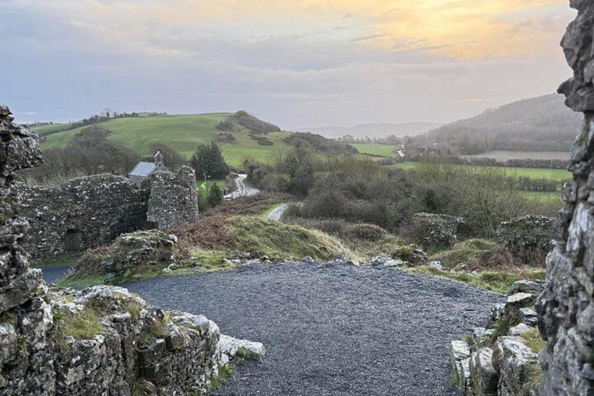 A rural landscape with a stone wall, a gravel area, and a winding road leading through rolling hills. 4