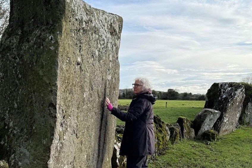A person touching a large stone monument in a grassy field with other stones in the background. 1