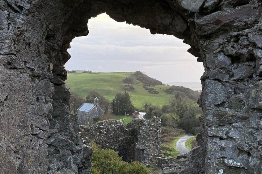 A stone archway overlooking a rural landscape with a winding road, a small building, and rolling hills. 3
