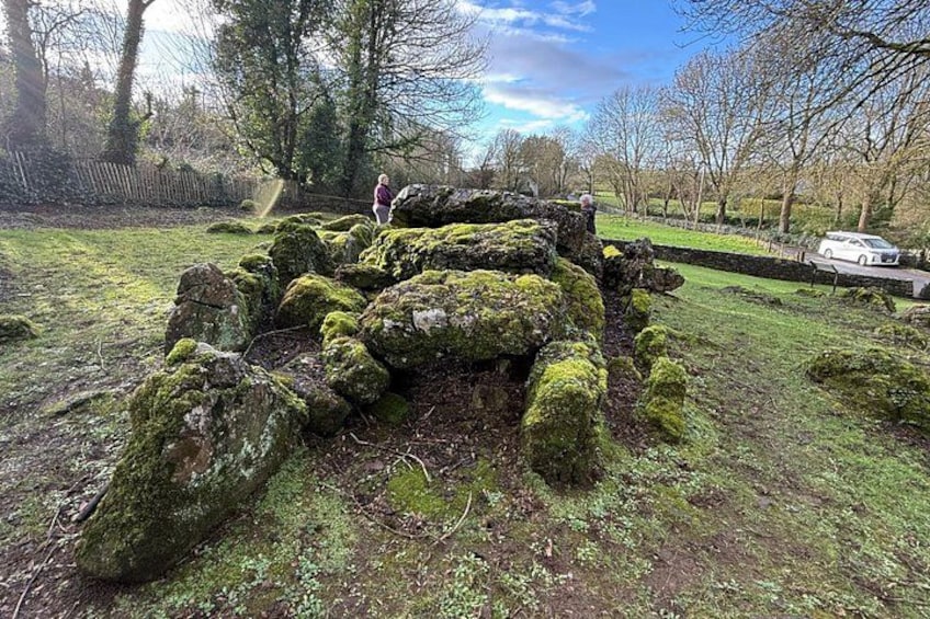 Une structure en pierre recouverte de mousse, située dans un parc, avec un sentier et des arbres en arrière-plan. 3