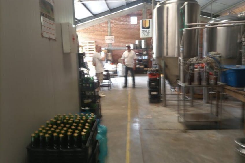 A brewery interior with stainless steel tanks, a brick wall, and a person in the background. 3