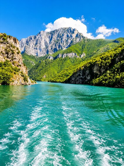 A turquoise lake surrounded by green hills and a mountain range. 2