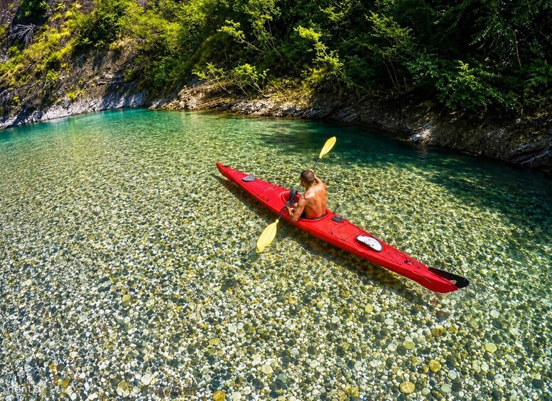 A person kayaking on clear water surrounded by rocks and greenery. 3