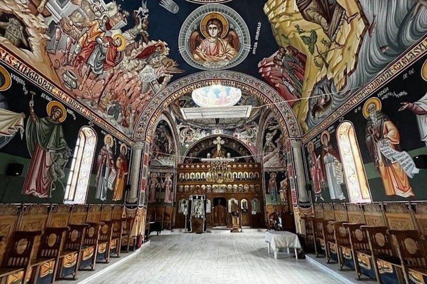 An ornate church interior with detailed frescoes, a central altar, and rows of pews. 1
