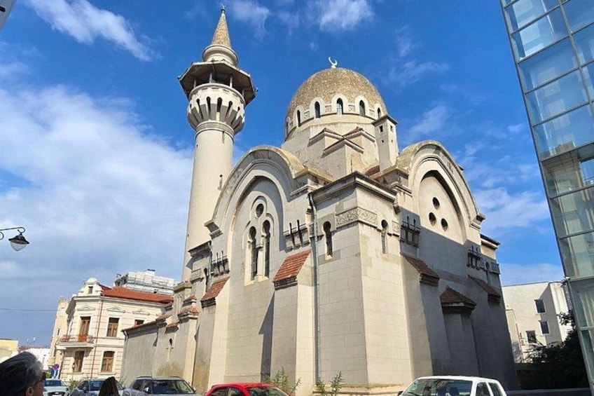A mosque with a tall minaret and a dome, surrounded by modern buildings. 4