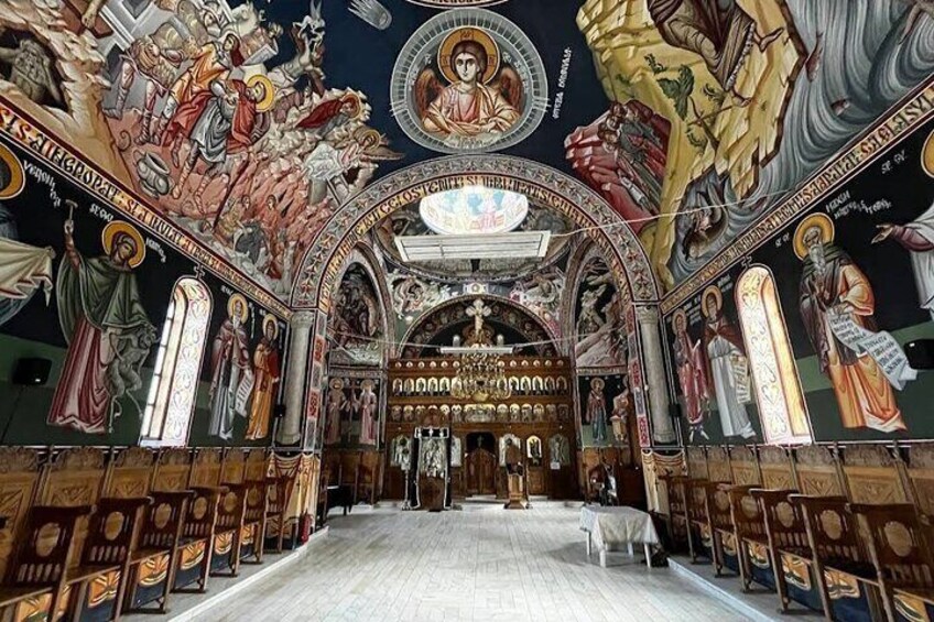 An ornate church interior with detailed frescoes, a central altar, and rows of wooden pews. 1