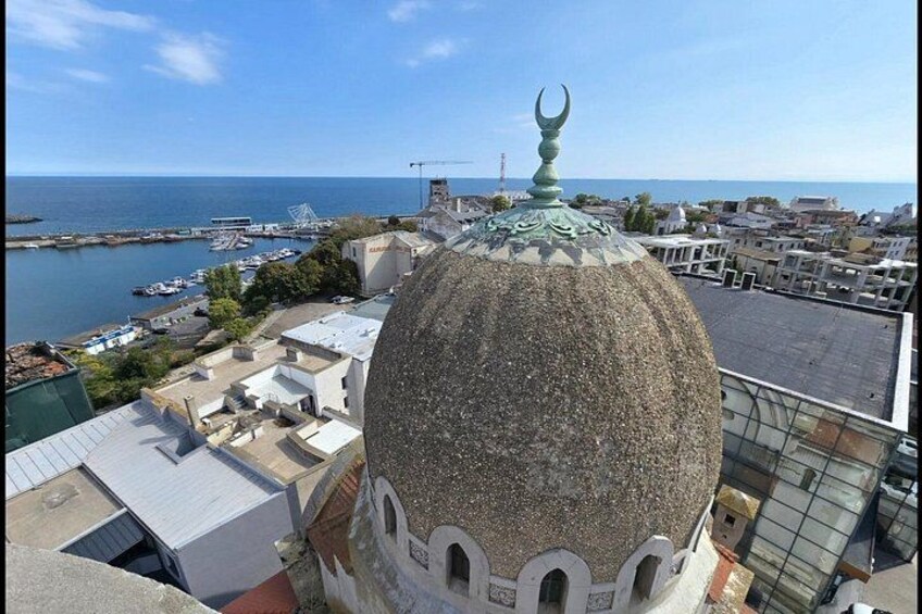 A domed building with a crescent moon finial, a harbor with boats, and a clear blue sky. 3
