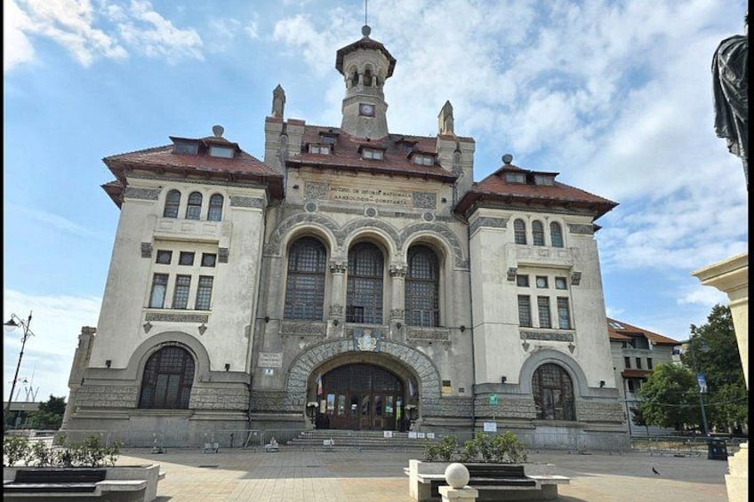 A historic building with a central arched entrance, a clock tower, and decorative stonework. 2