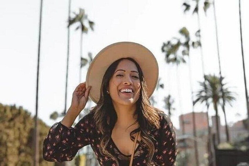 A person wearing a hat and a floral dress, standing outdoors with palm trees in the background. 5