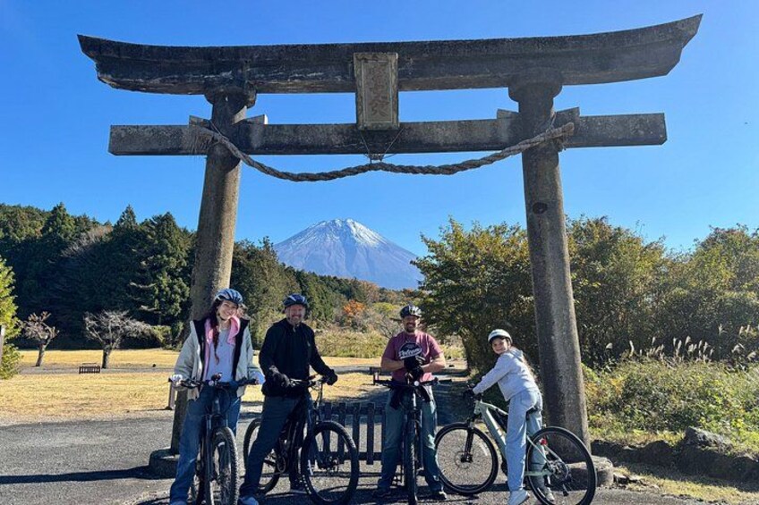 A group of people with bicycles near a wooden structure with a sign, in a park with trees and a mountain in the background. 5