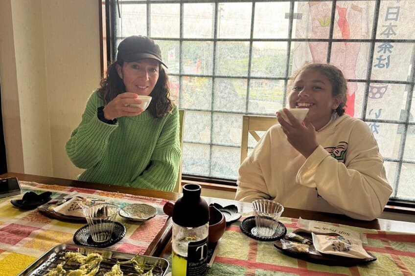 Two people sitting at a table with food and drink items. 2