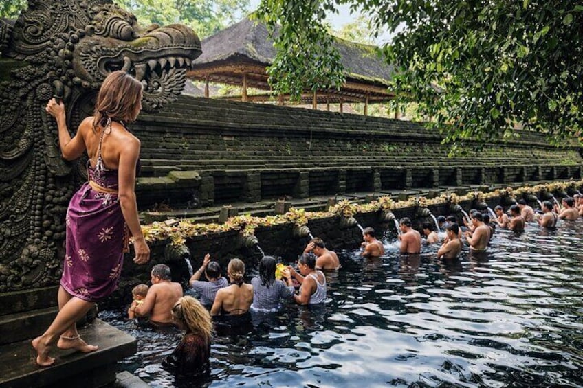 A woman in a purple dress standing on a stone platform by a water body with a dragon sculpture. 5