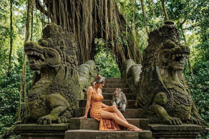 A woman sitting on stone steps with two stone lion statues on either side, surrounded by lush greenery. 4