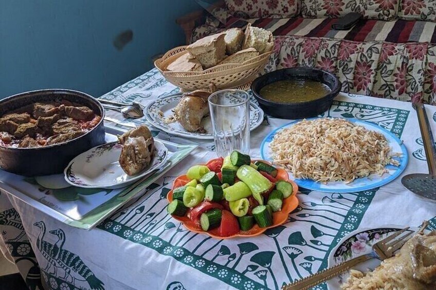 A table with various dishes including a bowl of stew, a plate of rice, and a salad with cucumbers and tomatoes. 5