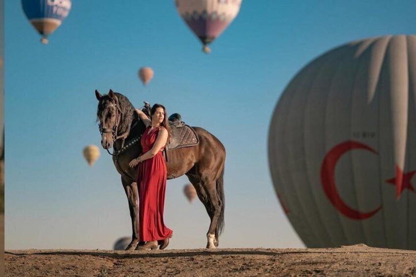 Een persoon in een rode jurk die paardrijdt, met luchtballonnen op de achtergrond. 1