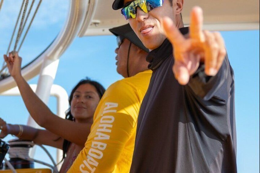 Una persona con una chaqueta amarilla y negra con la inscripción 'ALOHA BEACH' en la manga, señalando hacia la cámara. 2