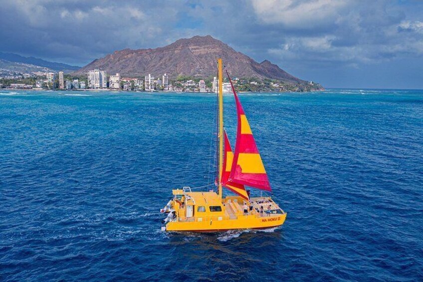 Un trimarán amarillo con velas de colores sobre un mar tranquilo, con una costa montañosa al fondo. 5