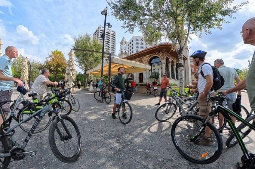 Un grupo de personas en bicicleta en un entorno exterior con árboles y un edificio al fondo. 2