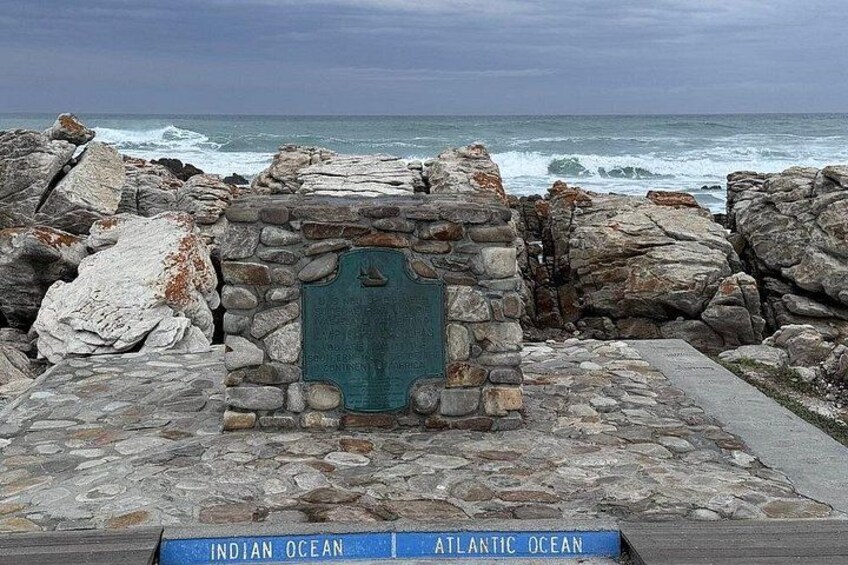 Een stenen monument met een plaquette aan een rotsachtige kustlijn, met de Indische Oceaan en de Atlantische Oceaan op de achtergrond. 5