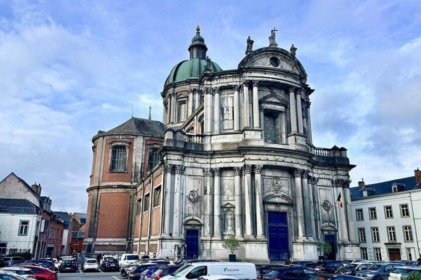 En historisk kirke med en kuppel og et klokketårn, omgivet af parkerede biler og bygninger. 3