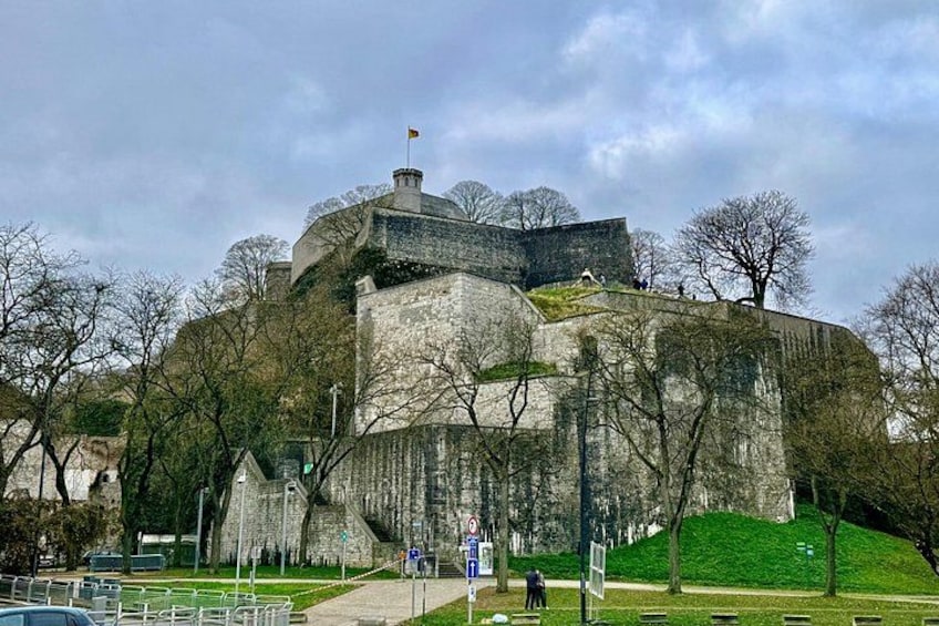Un castillo de piedra histórico con una bandera en la cima, rodeado de árboles y un área con césped. 2