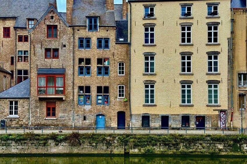 En række historiske bygninger med forskellige arkitektoniske stilarter, en stenvæg og et vandareal i forgrunden. 4