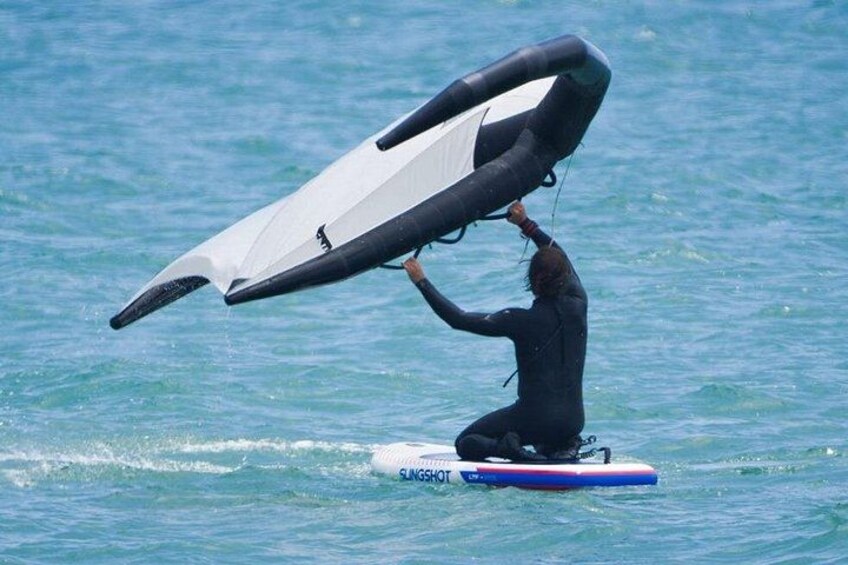 En person i våddragt holder et sejl over vandet, mens de står på et surfboard. 3
