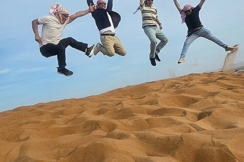 Four people jumping in the air above a sand dune landscape. 4