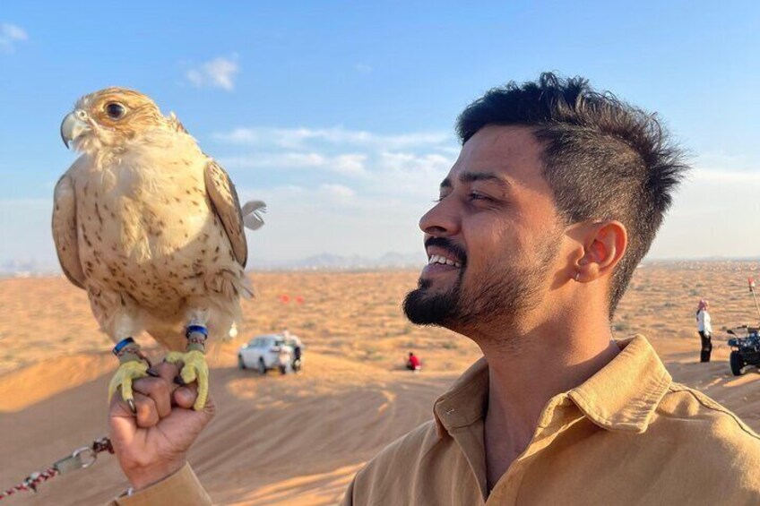 A person holding a falcon in a desert landscape with vehicles and people in the background. 3