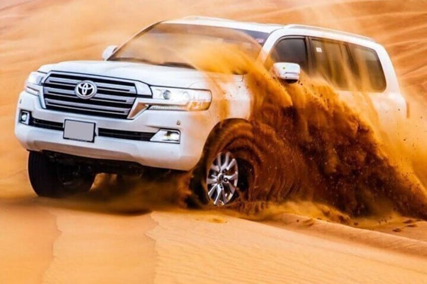 A white SUV driving through a sandy desert with a dust cloud behind it. 1