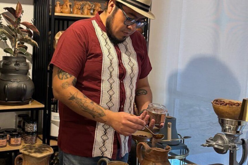 Une personne portant une chemise rouge et un tablier blanc, qui travaille avec des bocaux et un moulin à café. 4