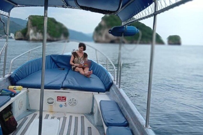 Une personne assise sur un bateau, un ordinateur portable sur les genoux, entourée d’une eau calme et d’îles verdoyantes à l’horizon. 2